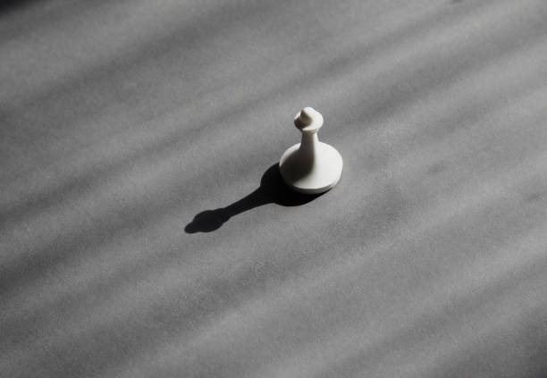 White pawn in bright sunlight casting a black shadow on a gray background, potential for transformation and advancement, beginning and development.