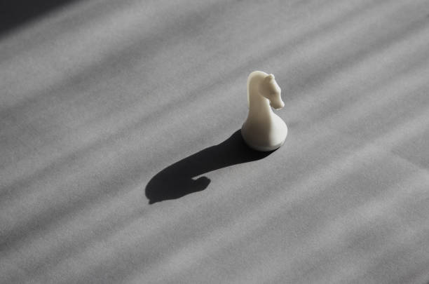 A white chess knight in bright sunlight casting a black shadow on a gray background, unconventional thinking, surprise and flexibility, freedom of thought, risk and adventurousness.
