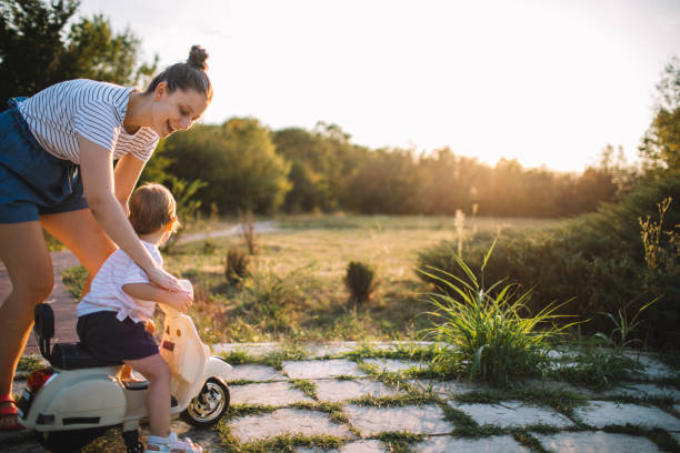 Mother watches as her toddler daughter rides an electric scooter.