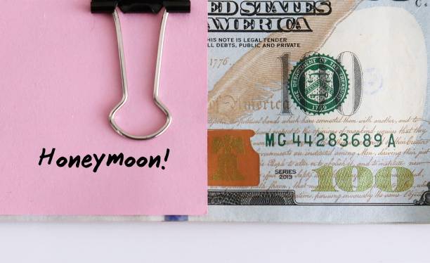 istock Cash money in dollars clipped with pink note written HONEYMOON on white background with copy space - concept of saving or planning budget for honeymoon trip 2178850607