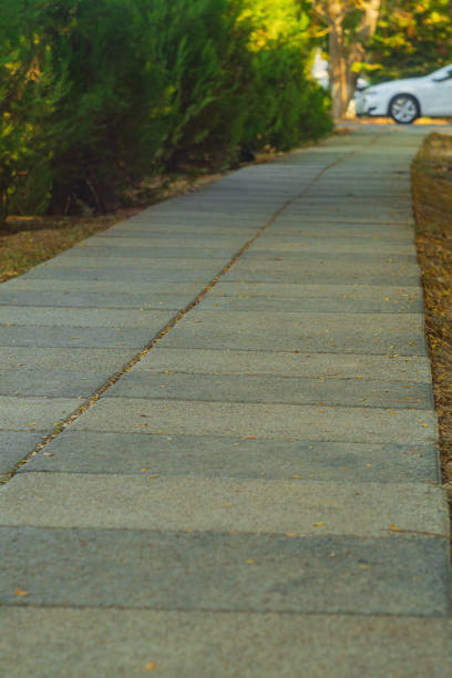 Surface of pedestrian walking path from low angle with perspective stretching into distance, in background resting on front of a white sedan car. Outdoor public spaces in an urban environment.