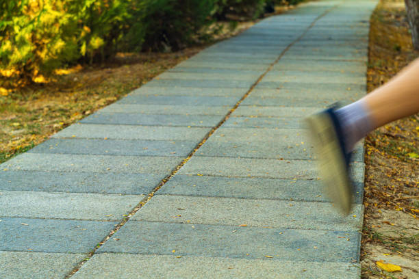 Pedestrian walking path with perspective stretching into distance, One leg of running white man washed out due to movement as he strays from straight path into unknown territory outside road.