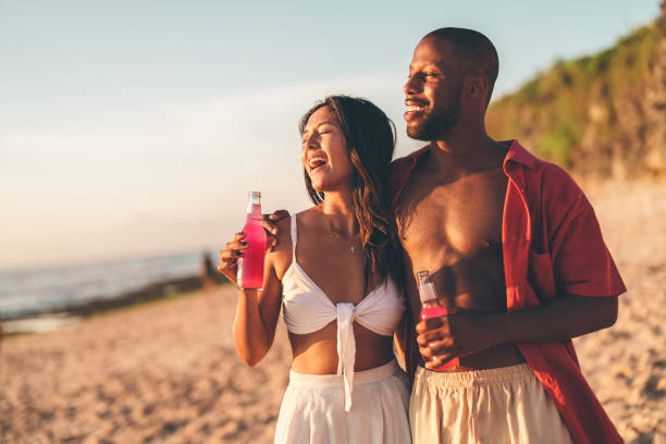 istock Walking the beach, a diverse couple shares a laugh, drinks in hand 2178853578