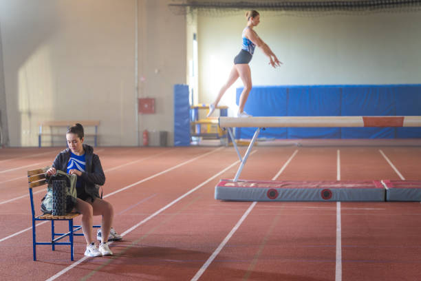 Gymnast young woman sitting on bench while opening bag in sports hall.