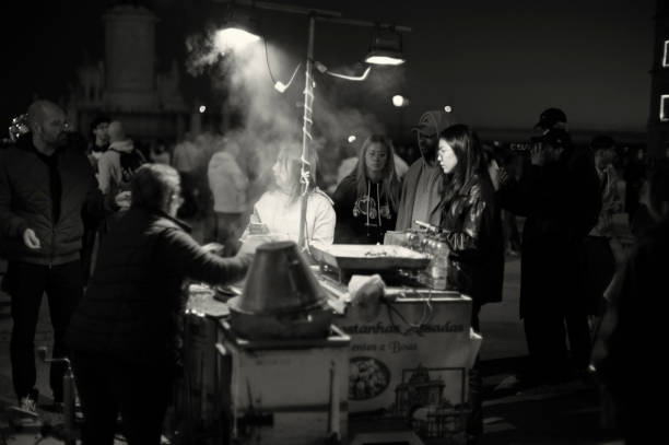 Lisbon, Portugal - December 23, 2023: A traditional roasted chestnuts vendor attends a client at the Praça do Comércio square in Lisbon downtown, during the Christmas season.