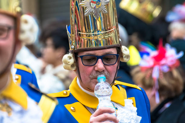 Man in blue and yellow uniform and copper helmet drinks from a water bottle during the Rosenmontag carnival parade in Cologne