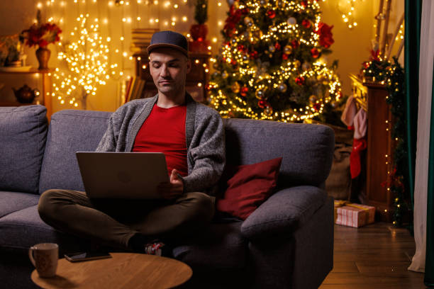 istock Young man, using laptop, sitting on the sofa with Christmas tree in the background 2178866299