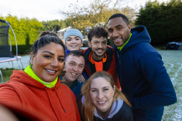 A medium point of view shot of a group of friends smiling for a selfie after a chilly morning run, bundled up in warm activewear with frost on the ground behind them. A moment of friendship and fun after a workout.\n\nVideos are available for this scenario.