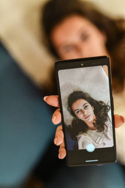 istock Young Beautiful Female Lying on Back and Taking Selfie to on Mobile Device While Looking Serious 2178871483