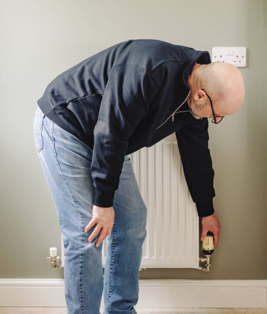 istock Middle aged bald man turning a radiator Thermostatic radiator valve down or up 2178873050