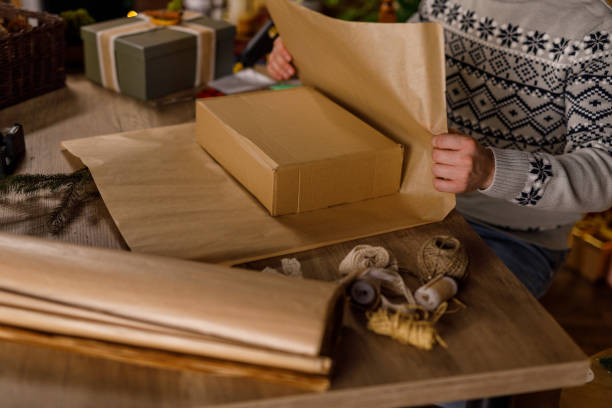 istock Young man wrapping a gift box in a rustic brown wrapping paper 2178876313