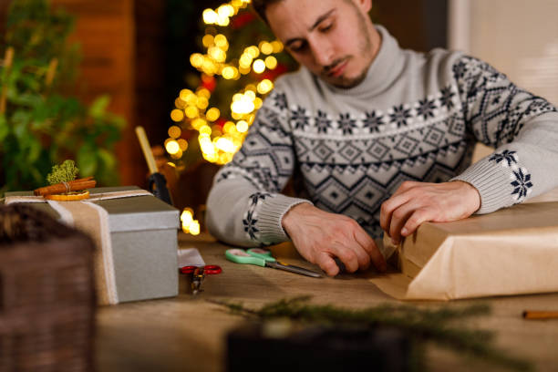 istock Young man folding edges of a rustic brown paper that he is using to wrap a Christmas gift box 2178876319