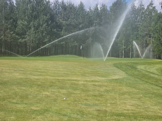 istock Watering the lush green golf course with sprinklers under a clear blue 2178890119