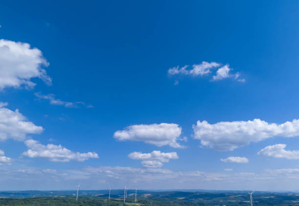 A clear blue sky dotted with fluffy white clouds over rolling green hills, showcasing wind turbines in the distance, symbolizing renewable energy and nature's beauty.