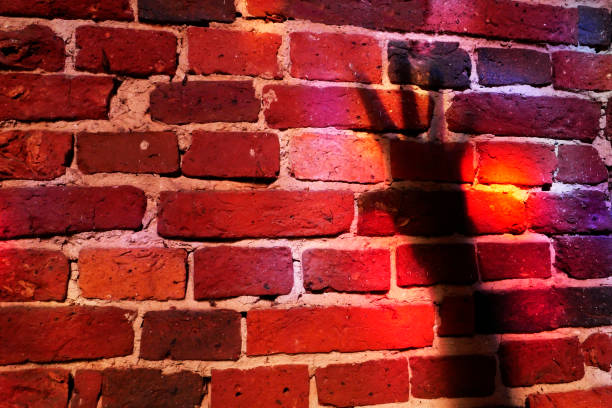 A red brick wall with red reflections from a stained glass window. The shadow of an outstretched arm with spread fingers