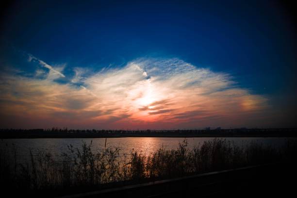 Sunset sky and clouds over lake with grass in foreground