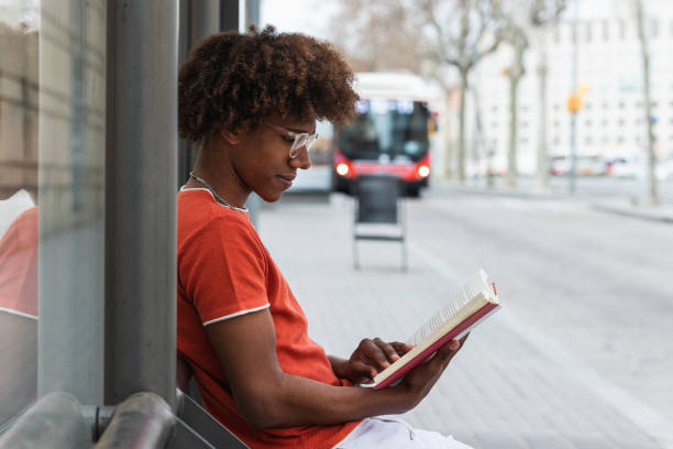 istock Calm young black male reading novel at bus stop 2178952746