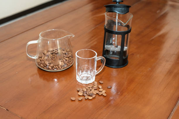 Brewing method French press coffee maker, with beans on coffee server pot, french press, glass and Scattered coffee beans on the wooden table, making coffee homemade.