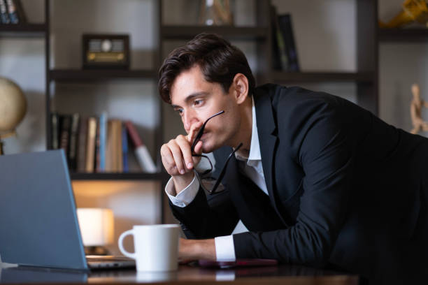 istock The young businessman in black suits looks thoughtful while reading his e-mails from his laptop. 2178963752