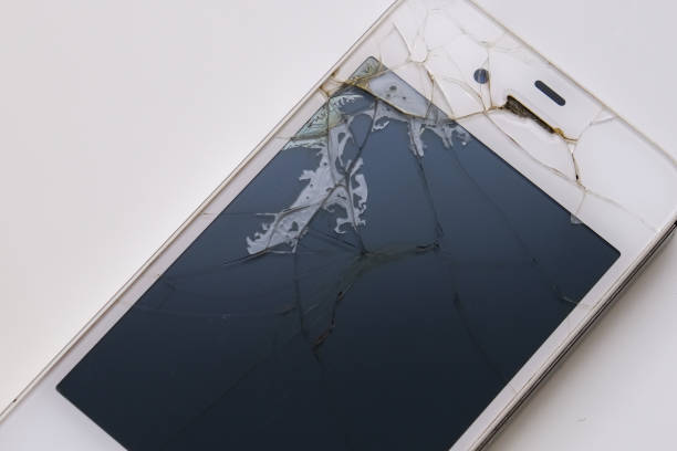 A broken cell phone with a cracked screen on a wooden table. The phone is in pieces, and the screen is shattered. Concept of loss and despair, as the phone is no longer functional
