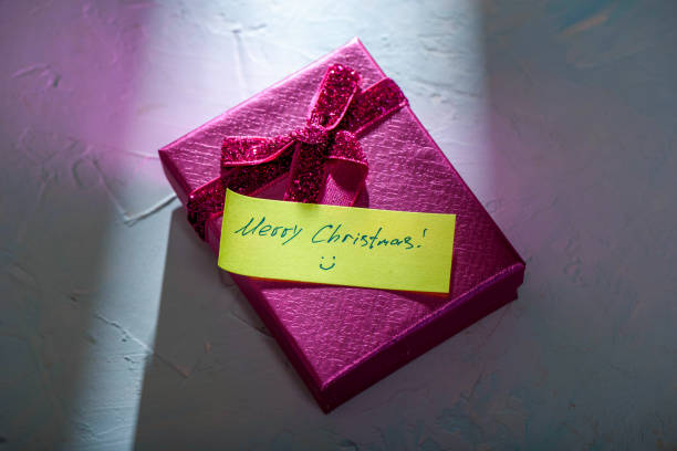 A vibrant pink gift box with a yellow note Merry Christmas on a textured background, symbolizing joy and surprise.