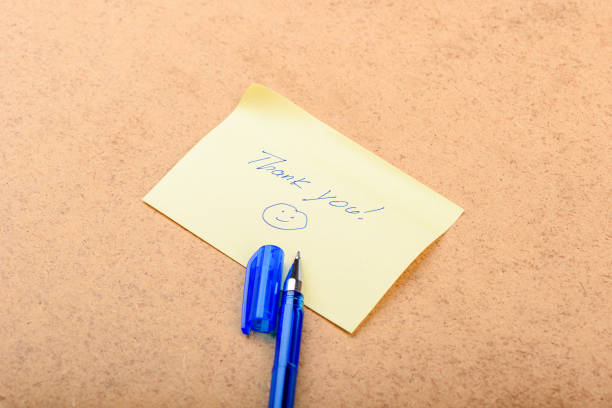 A handwritten note saying Thank you with a smiley face, placed on a wooden background.