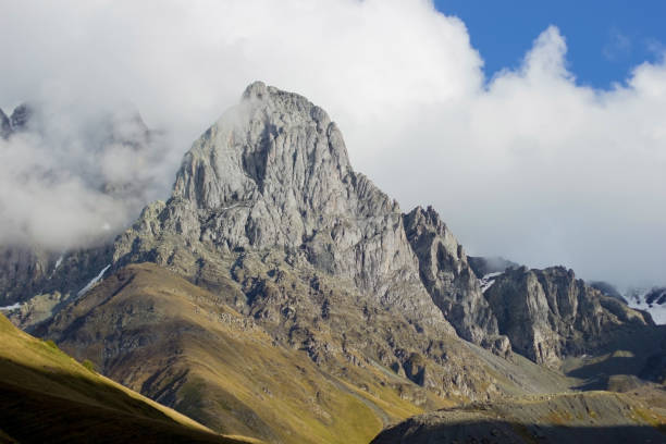 istock A towering mountain peak rises through the mist, revealing its rugged rock formations under a bright sky. The scene captures the raw beauty and grandeur of nature in a mountainous landscape 2178988784