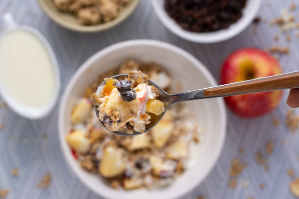Top view of  a scoop of Yogurt Parfait mixed with granola, oat and fruit in a spoon with the bowl of the parfait and ingredients blurred in the background