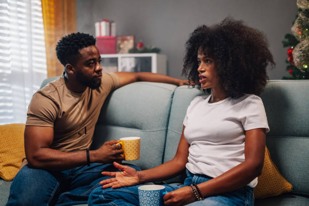 Engaged multiracial couple talks holding coffee mugs over Christmas decor
