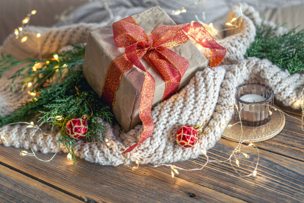 Christmas composition with a festive gift. Christmas concept. High quality photo. Christmas gift with burning candle. On a wooden table. Knitted sweater. Christmas tree branches.