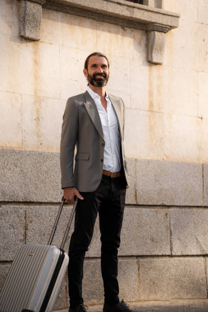 istock Businessman smiling holding suitcase looking away from camera 2179029678