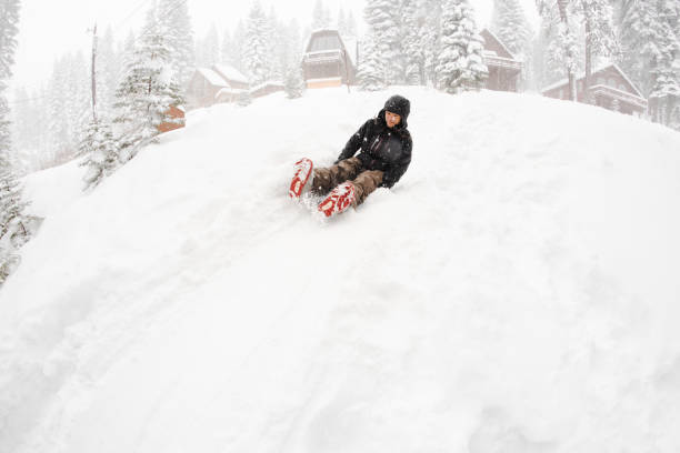 Young man with long hair sledding in the snow. Happy and cheerful. Wearing warm clothing during a snow storm