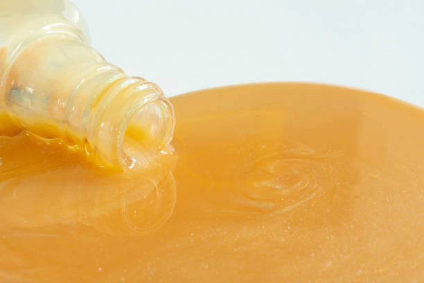 A close up image of a spilt bottle of gold colored finger nail polish on a white background.