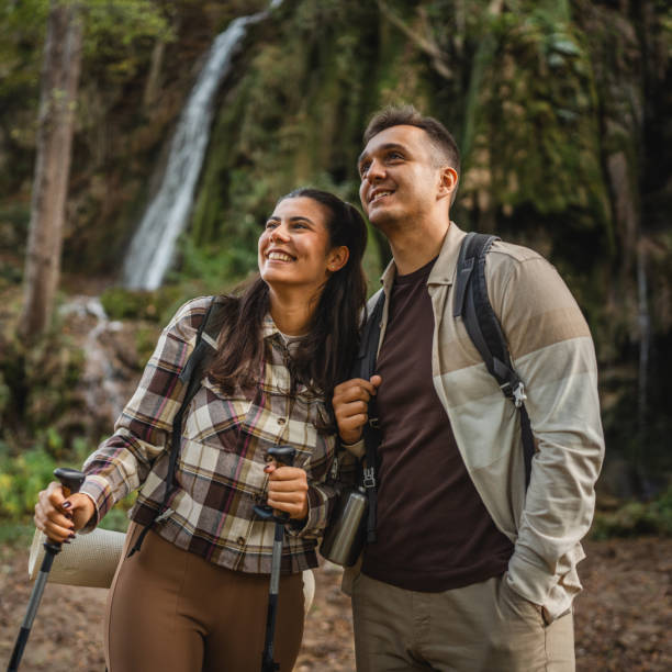 istock hiker couple explore forest around waterfall with hiking sticks 2179046539
