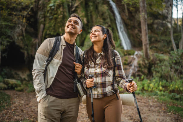 istock hiker couple explore forest around waterfall with hiking sticks 2179046944
