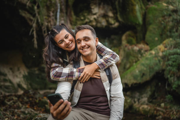 istock hugged hiker couple backpackers in front waterfall and use cellphone 2179047319