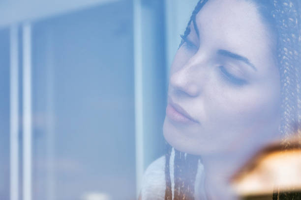 istock Young woman looking through window reflecting on life 2179072835