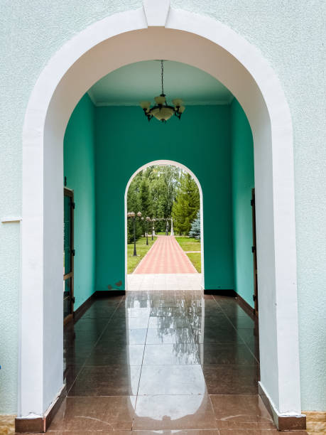A grand hallway featuring an elegantly designed archway gracefully opens to a stunning park area, creating a seamless transition that beautifully connects the indoor space with the vibrant outdoors