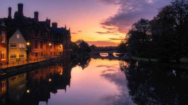 Buildings reflected in the still waters of the River Great Ouse at sunrise in Bedford, England with the Town Bridge in the distance