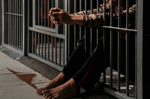 istock hands of a prisoner behind prison bars on black background 2179090979