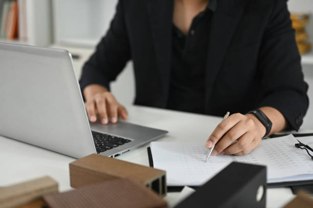 istock Architect working on laptop at a desk with material samples and house model in the foreground 2179105254