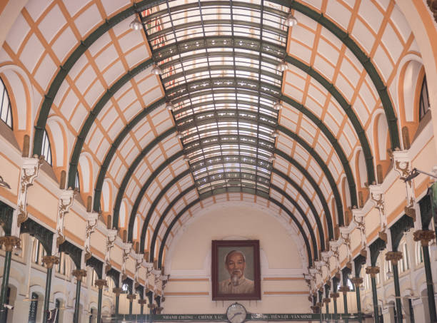 Ho Chi Min City (or Saigon) Vietnam - December 8th, 2023: The interior atrium inside the central post office, a French colonial building designed by the famous architect Gustav Eiffel. At the end of the hall there is a clock and a huge painting of Ho Chi Min. \nToday it is a popular destination for tourists. The post office is still functional and tourists can send out postcards and letters even today.