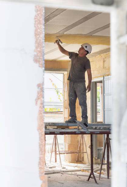 istock Craftsman in grey clothes working inside a room standing on scaffoldings during construction 2179106164