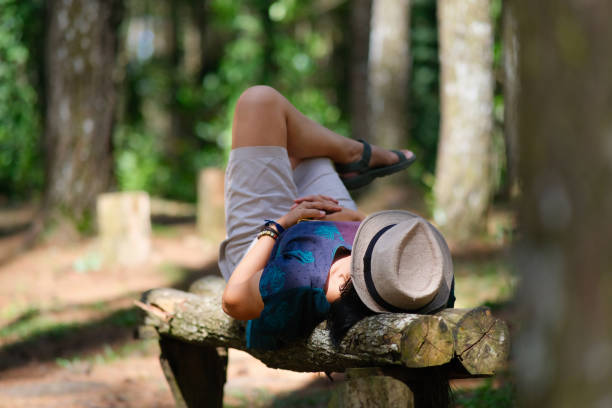 An old man sits in the garden, resting and protecting his head from the sun.