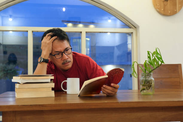 istock Man sitting and reading a book with very tired facial expression 2179107699