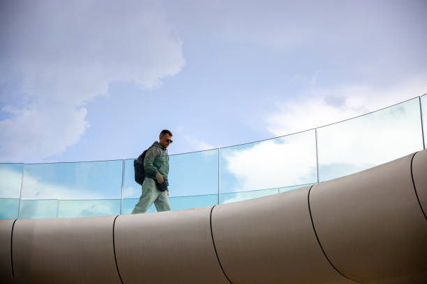 Man with backpack walking along a curve, modern structure, view from below on the blue sky