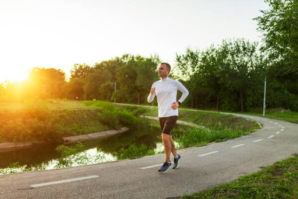 istock Young man running in park by the river at sunset 2179151815