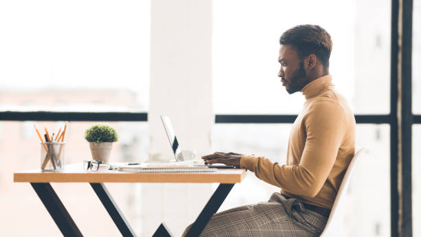 istock Afro businessman working on laptop in modern office, side view 2179153401
