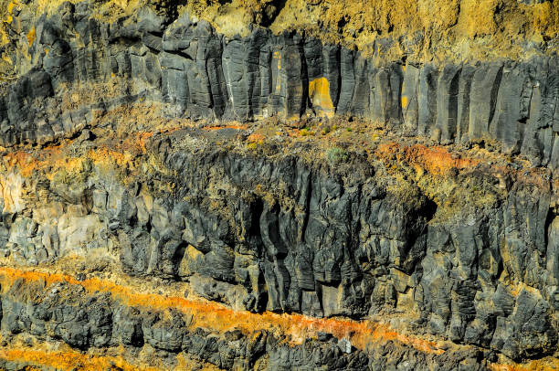 A rocky cliff with a yellowish-brown color. The rocks are jagged and rough, giving the impression of a harsh and rugged environment. The contrast between the dark rocks