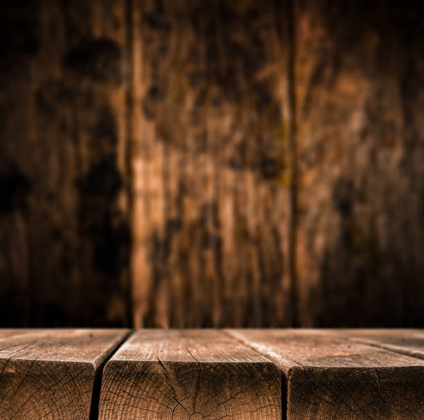 A close-up of a rustic wooden surface with visible cracks, moss, and rough texture, set against a blurred, dark wooden background. The image has a natural, earthy atmosphere and is perfect for themes related to nature, outdoors, or craftsmanship.